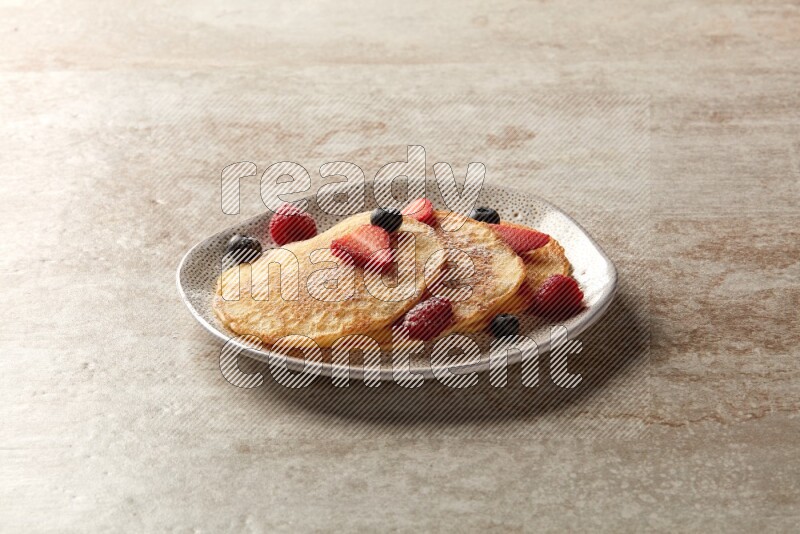 Three stacked mixed berries pancakes in an irregular plate on beige background