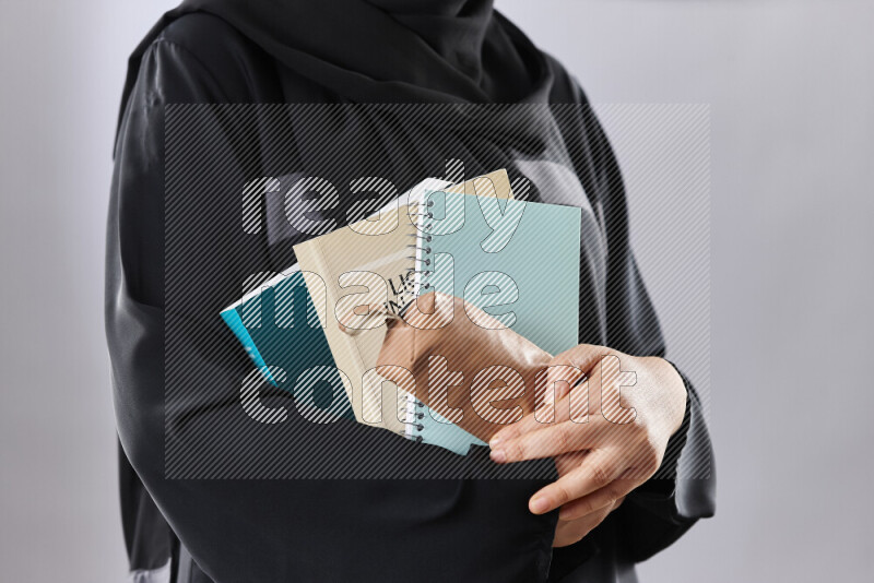 A woman in abaya holding books and a board in different positions (back to school)