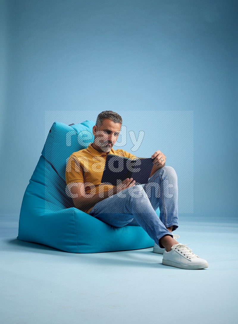 A man sitting on a blue beanbag and reading a book