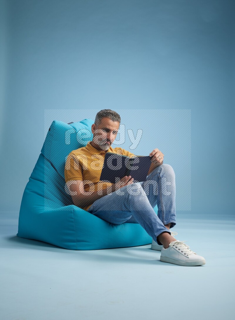 A man sitting on a blue beanbag and reading a book
