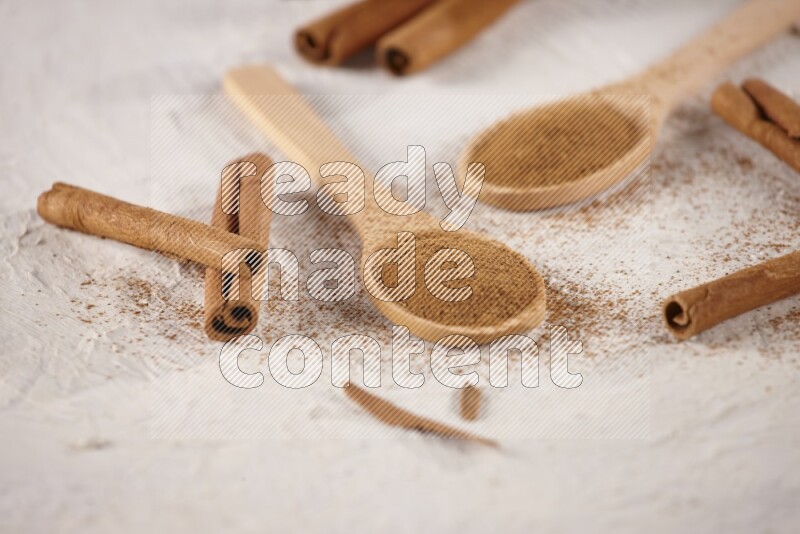 Two wooden spoons full of cinnamon powder with cinnamon sticks on white background