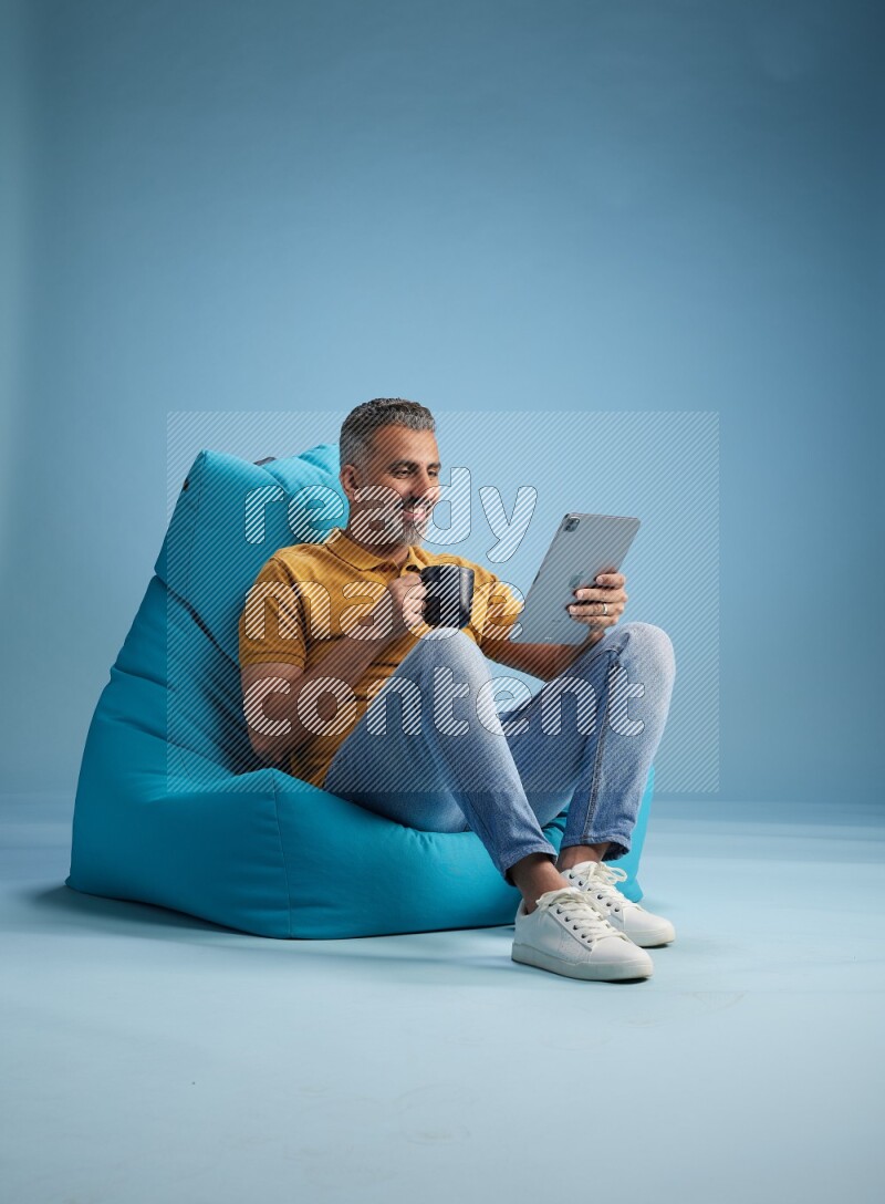 A man sitting on a blue beanbag and drinking coffee