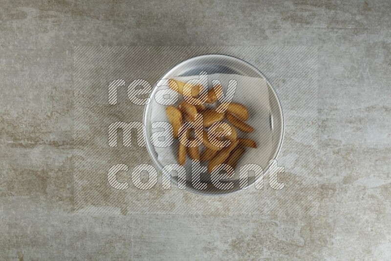 wedges potato on parchment paper in a stainless steel round tray on grey textured counter top
