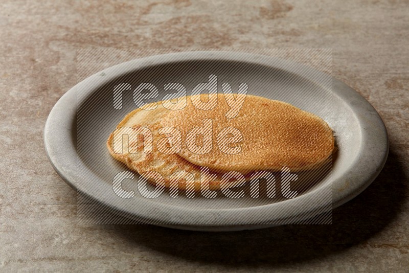 Two stacked plain pancakes in a grey plate on beige background
