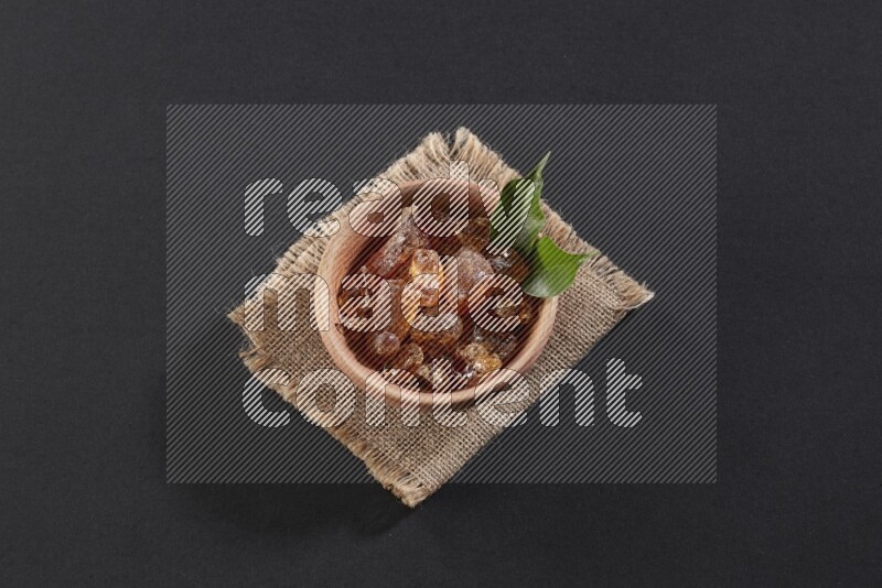 A wooden bowl full of gum arabic on a piece of burlap on black flooring