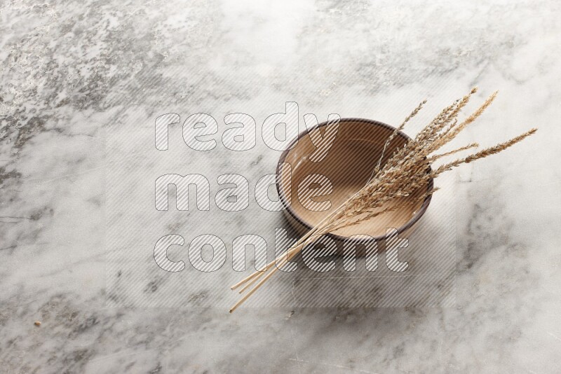 Wheat stalks on beige pottery oven bowl on grey marble background