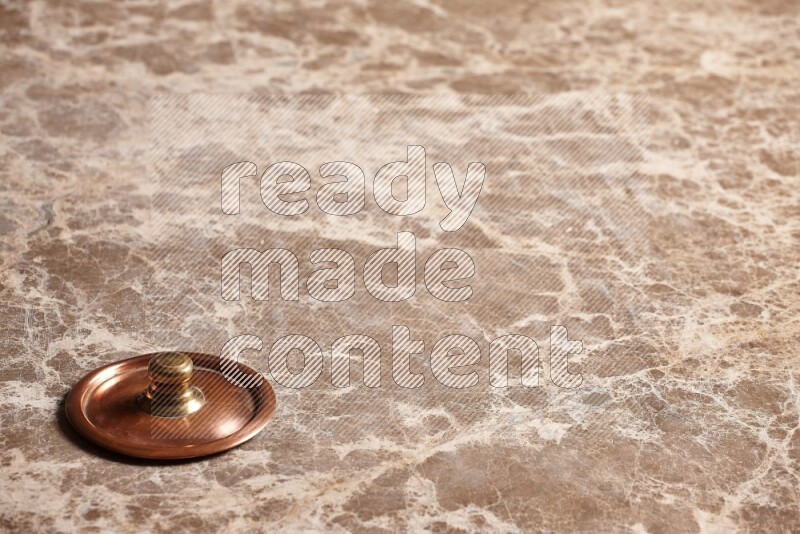 A small copper pot lid on beige marble background