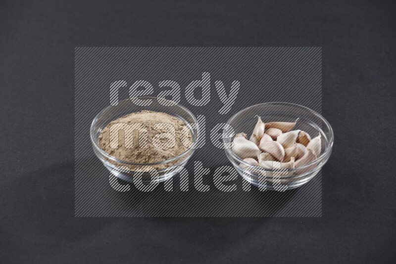 وعاءان زجاجيان احدهما ممتلئ ببودرة الثوم والأخر ممتلئ بفصوص الثوم علي خلفية سوداء