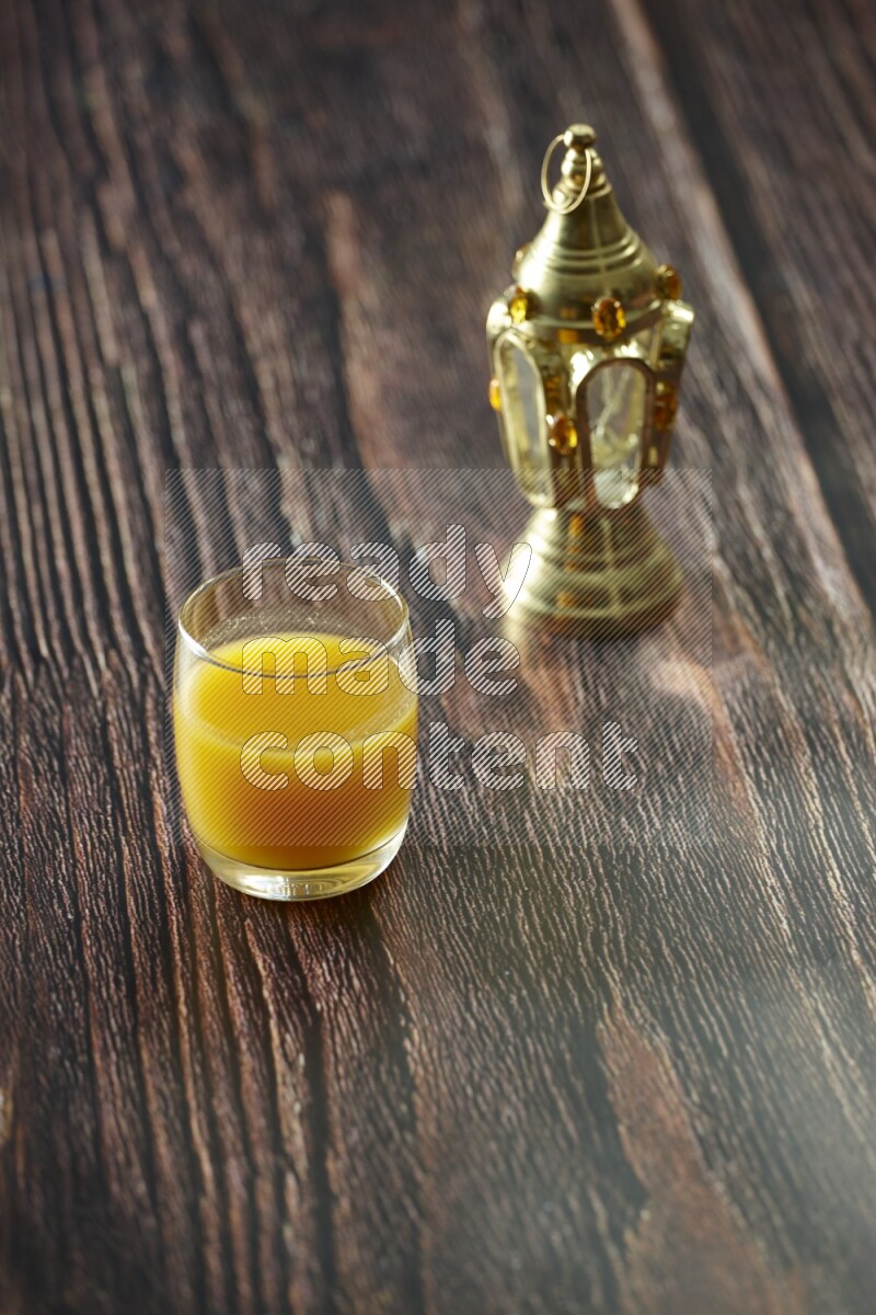 A golden lantern with different drinks, dates, nuts, prayer beads and quran on brown wooden background