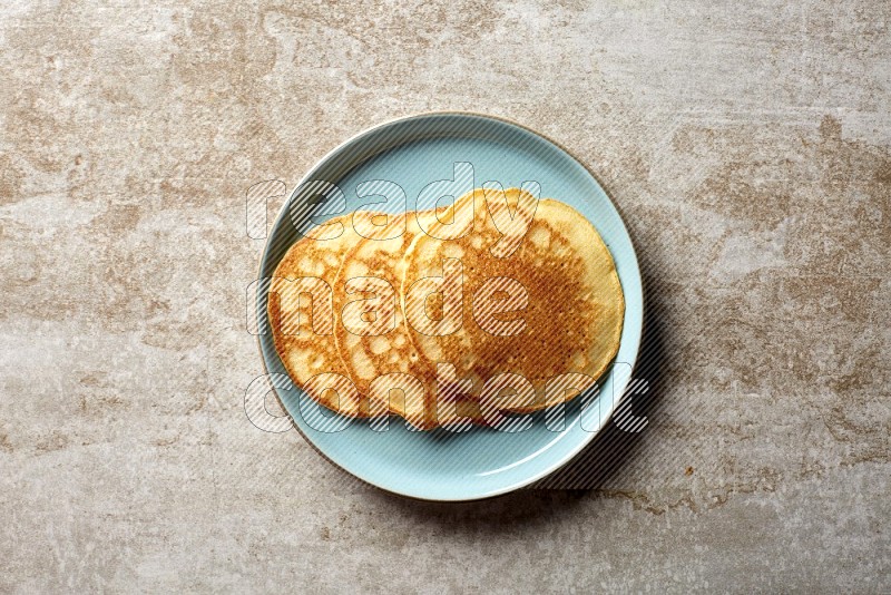 Three stacked plain pancakes in a blue plate on beige background