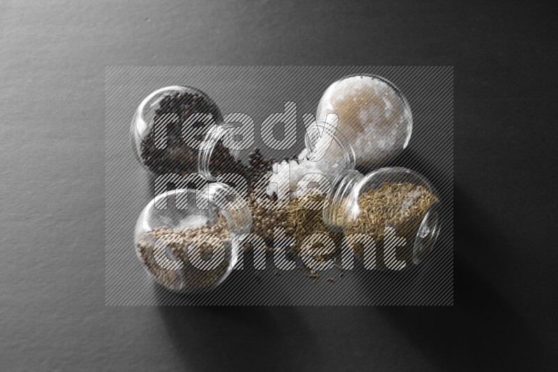 ملح وفلفل أسود وفلفل أبيض وكمون في أوعية زجاجية علي خلفية سوداء