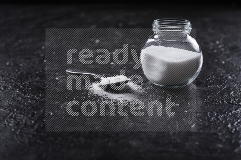 A glass jar full of fine table salt on black background