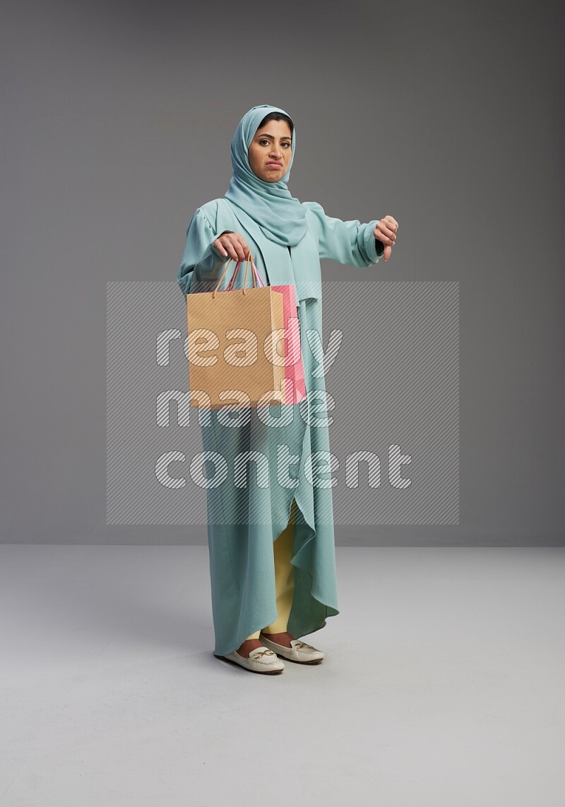 Saudi Woman wearing Abaya standing holding shopping bag on Gray background