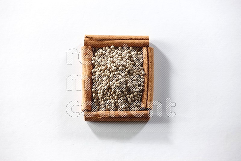 A single square of cinnamon sticks full of white pepper on white flooring