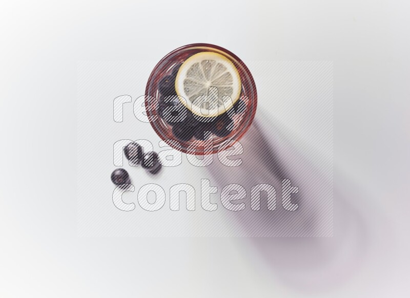 Blue transparent glass filled with blueberries decorated with lemon slices on a white background