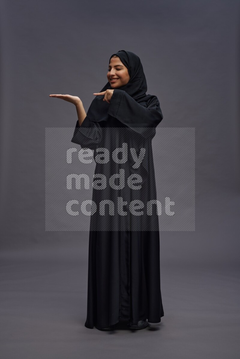 Saudi woman wearing Abaya standing interacting with the camera on gray background
