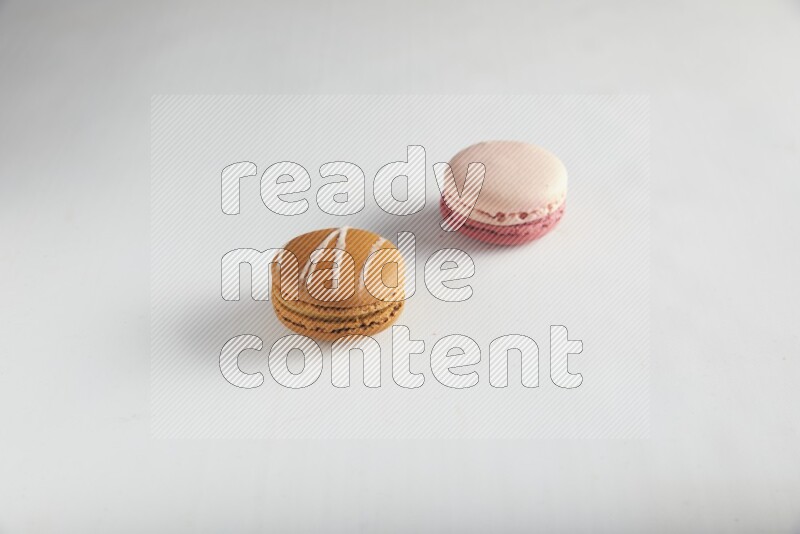 45º Shot of of two assorted Brown Irish Cream, and Pink Litchi Raspberry macarons on white background