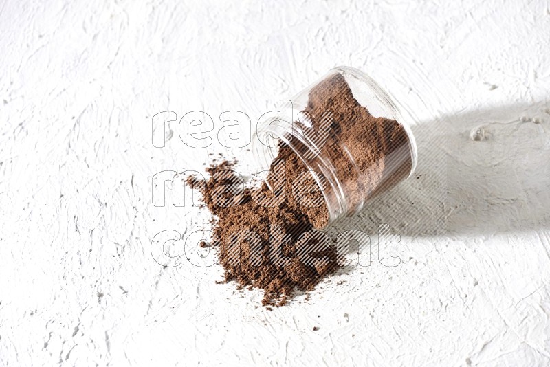 A flipped glass jar full of cloves powder on a textured white flooring