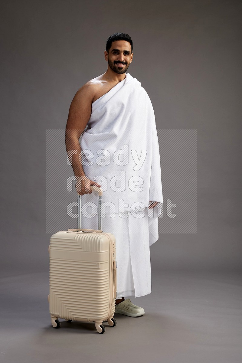 A man wearing Ehram Standing holding traveling bag on gray background