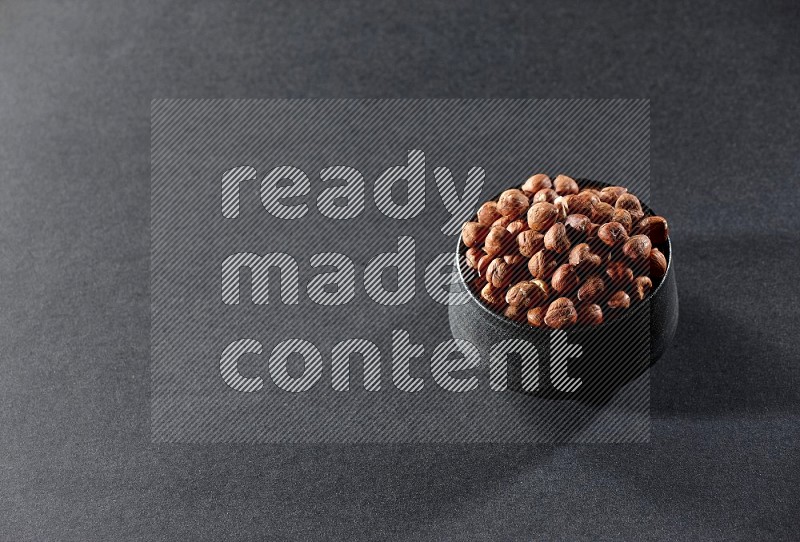 A black pottery bowl full of peeled hazelnuts on a black background in different angles