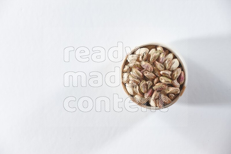 A beige ceramic bowl full of peeled pistachios on a white background in different angles