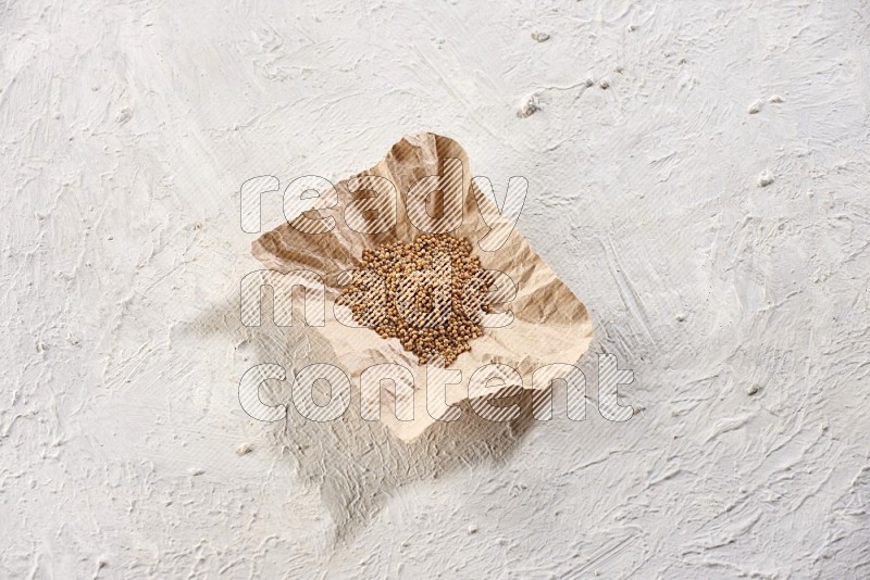 A crumpled piece of paper full of mustard seeds on a textured white flooring in different angles