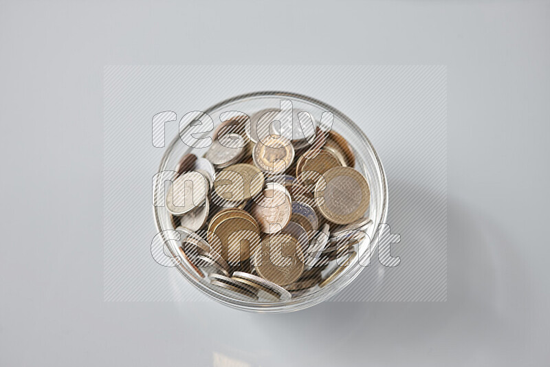 Random old coins in a glass bowl on grey background