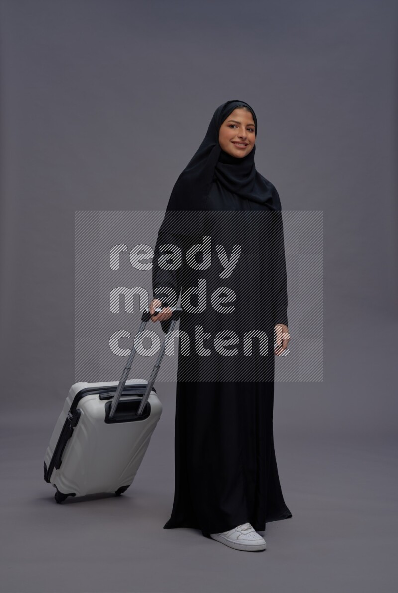 Saudi woman wearing Abaya standing holding bag on gray background