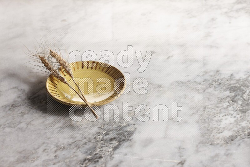 Wheat stalks on multicolored pottery plate on grey marble background