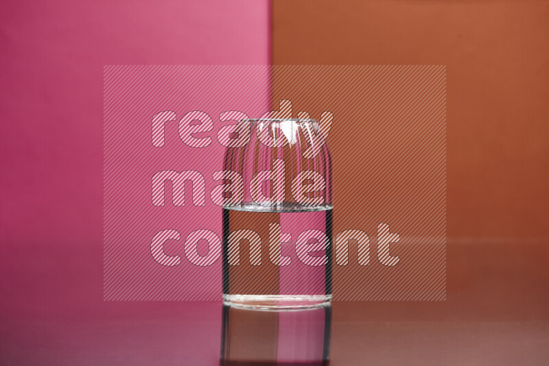 The image features a clear glassware filled with water, set against pink and dark orange background