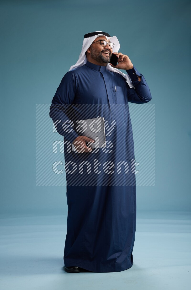 Saudi Man with shimag Standing talking on phone on blue background