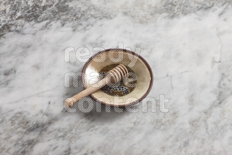 Decorative pottery plate with wooden honey dipper in it on grey marble background