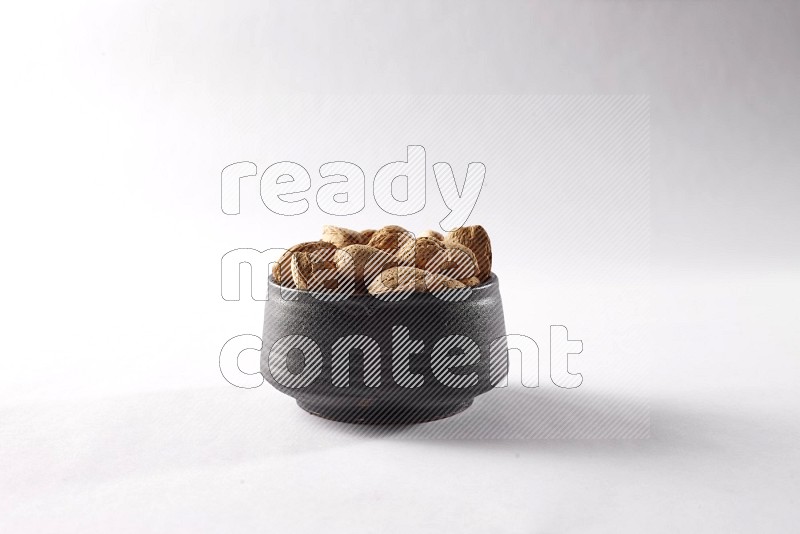 Almonds in a black pottery bowl on white background