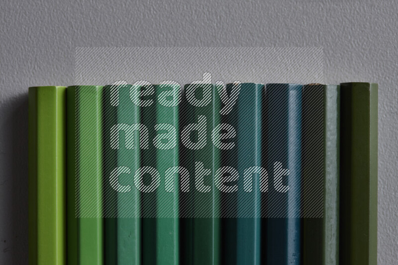 A collection of colored pencils arranged showcasing a gradient of green hues on grey background