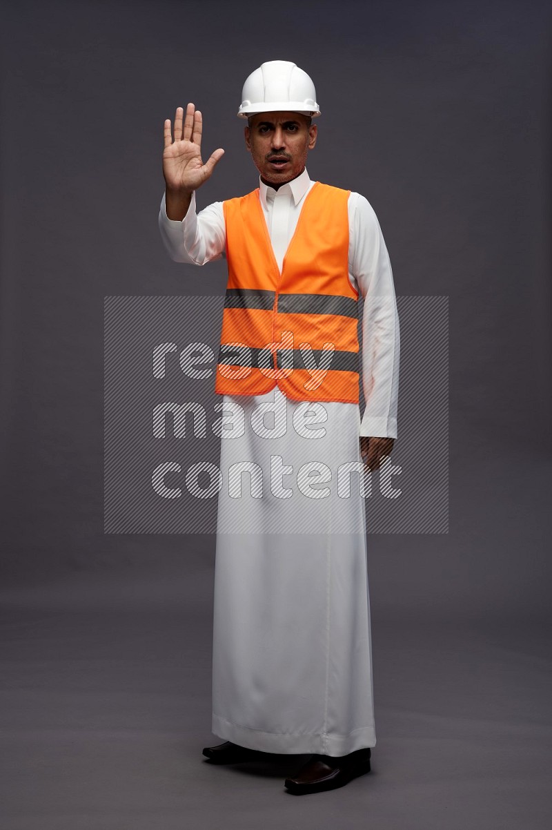 Saudi man wearing thob with engineer vest standing interacting with the camera on gray background