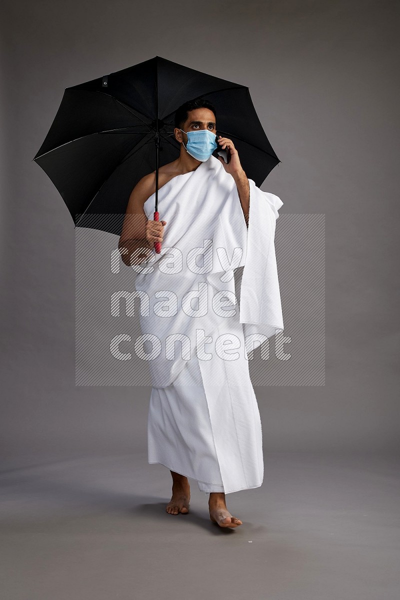 A man wearing Ehram and mask Standing holding umbrella on gray background on gray background