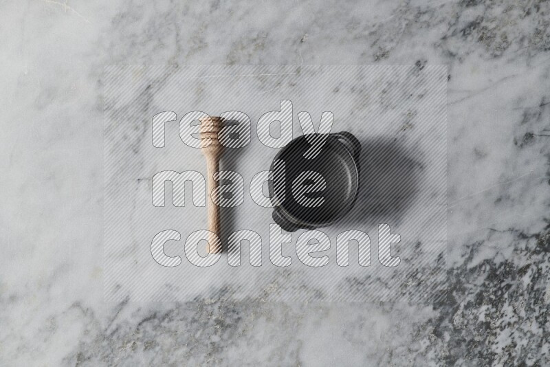 Black pottery bowl with wooden honey dipper on the side on grey marble background