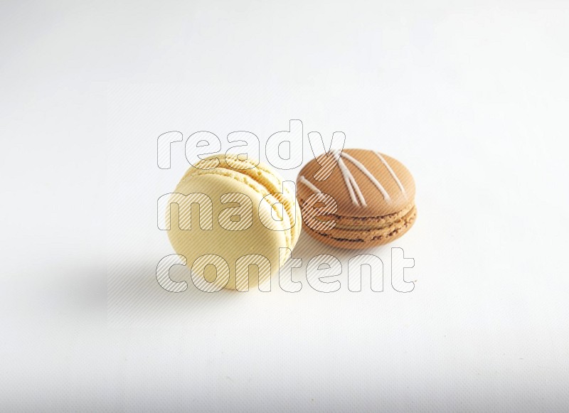 45º Shot of of two assorted Brown Irish Cream, and Yellow Vanilla macarons on white background