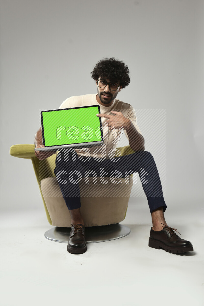 A man wearing casual sitting on a chair showing a laptop screen on white background