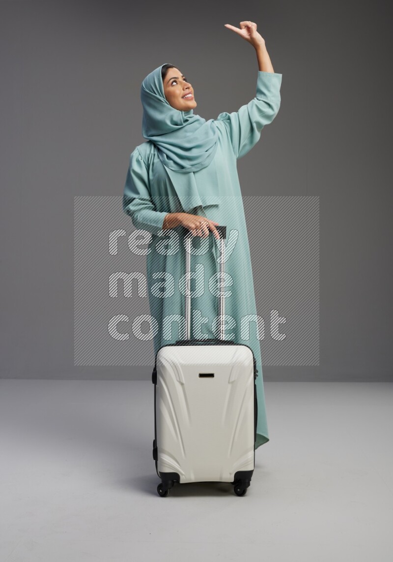Saudi Woman wearing Abaya standing holding Travel bag on Gray background