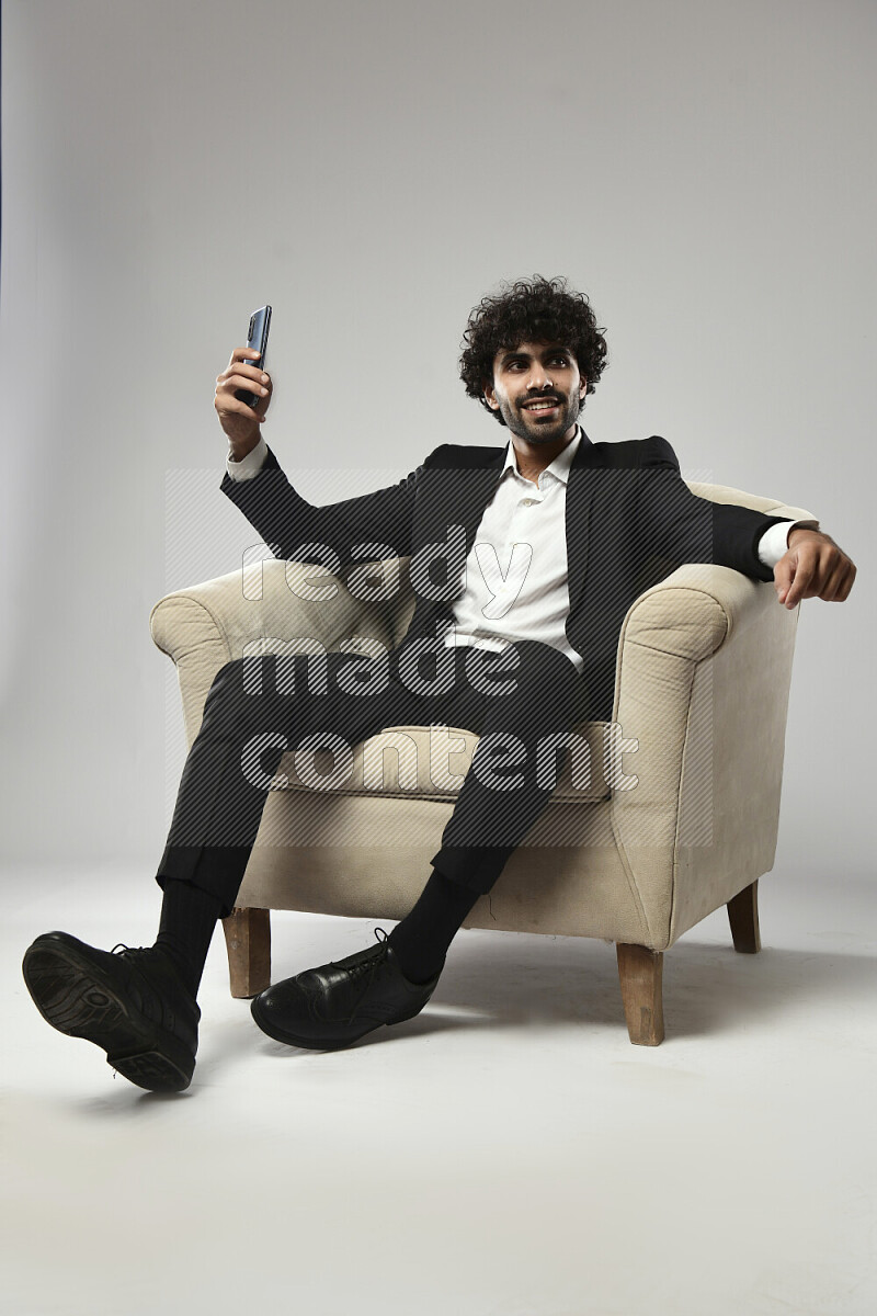 A man wearing formal sitting on a chair taking a selfie on white background