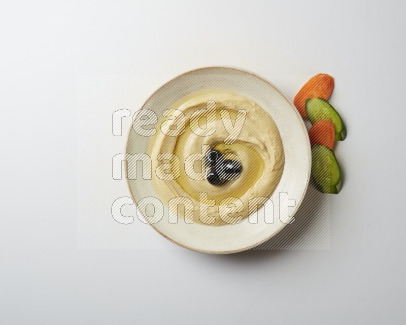 Hummus in a pottry plate garnished with black olives on a white background