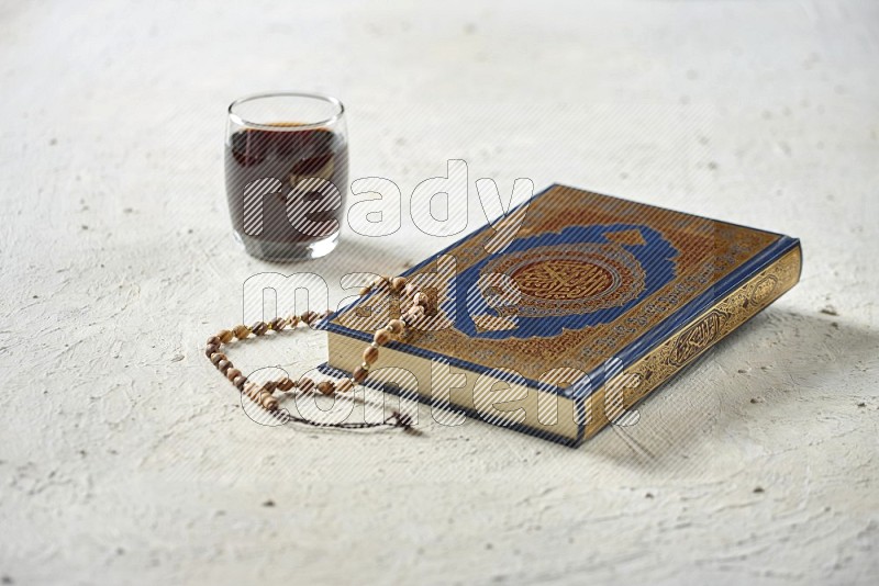 Quran with dates, prayer beads and different drinks all placed on textured white background