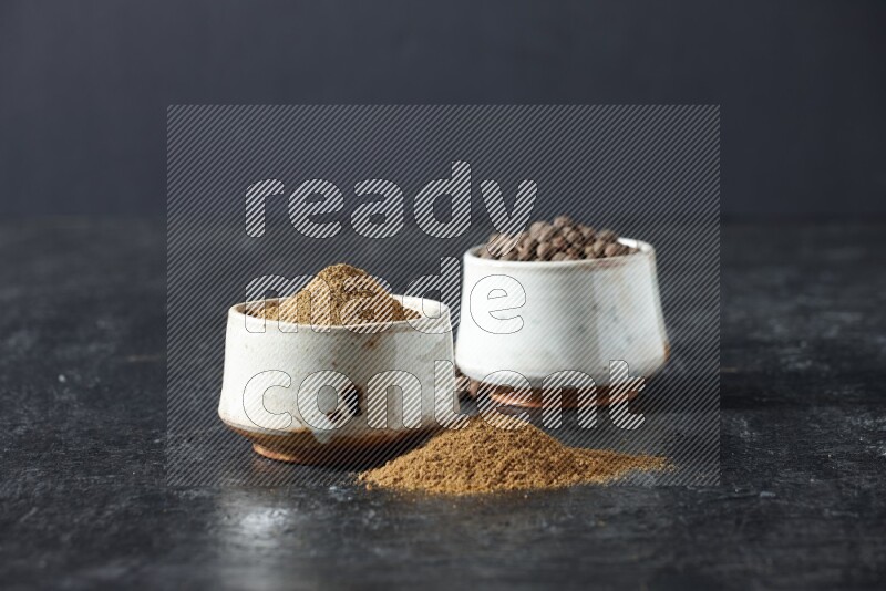 وعاءان بيج، أحدهما ممتلئ ببودرة بهار الفلفل الحلو والآخر بالحبوب وكلاهما متناثران على خلفية سوداء