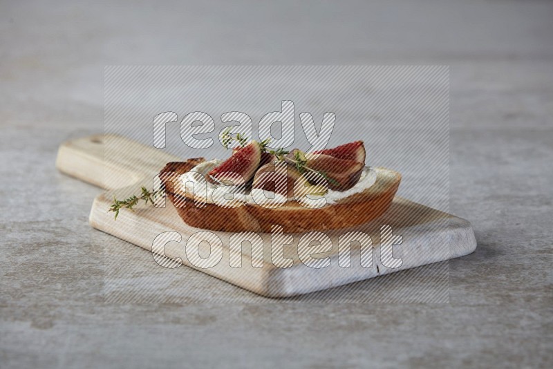 quarters of figs with cream cheese on toasted sourdough slice on a wooden board on textured grey background