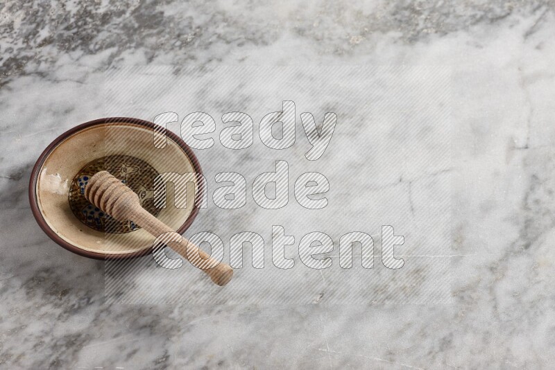 Decorative pottery plate with wooden honey dipper in it on grey marble background