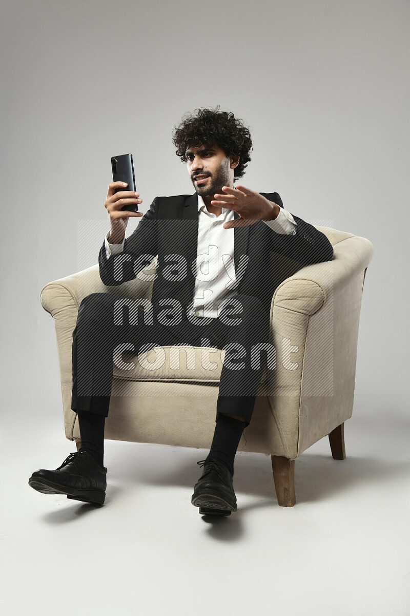A man wearing formal sitting on a chair shooting with his phone on white background