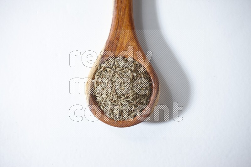 A wooden ladle full of cumin seeds on a white flooring