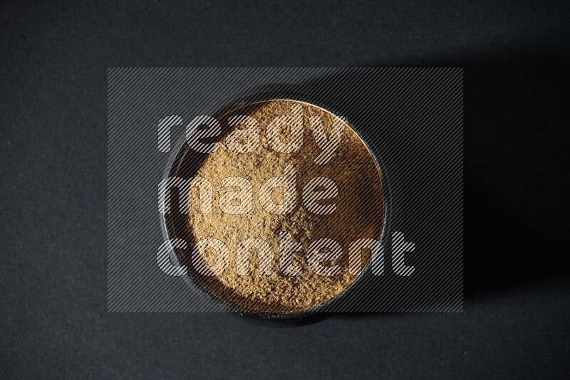 وعاء فخاري أسود ممتلئ ببودرة الكمون على خلفية سوداء