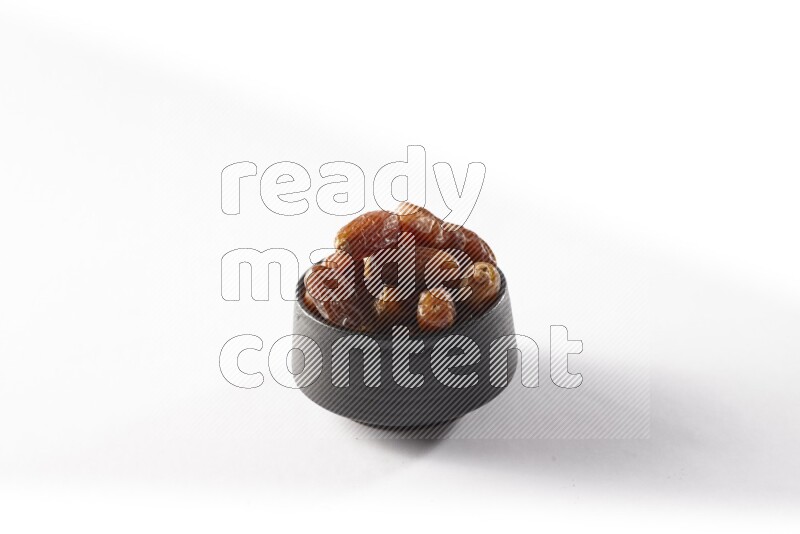 Dates in a black pottery bowl on white background